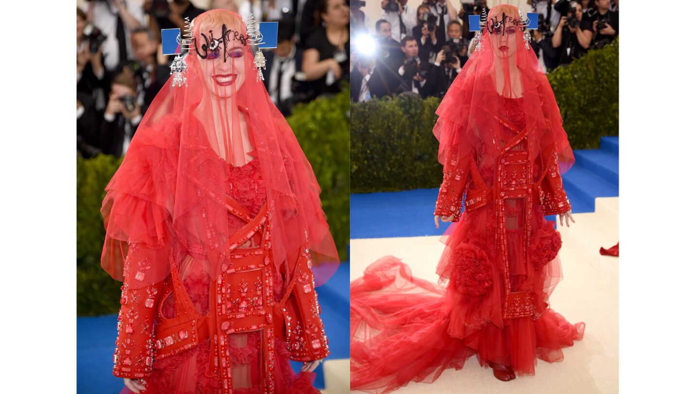 Co-chairperson Katy Perry at the Met Gala in a crimson red Maison Margiela Artisanal wool coat over a tulle and chiffon gown. It was designed by John Galliano. We're not sure about the provenance of the headpiece but it certianly qualifes as avant-garde.