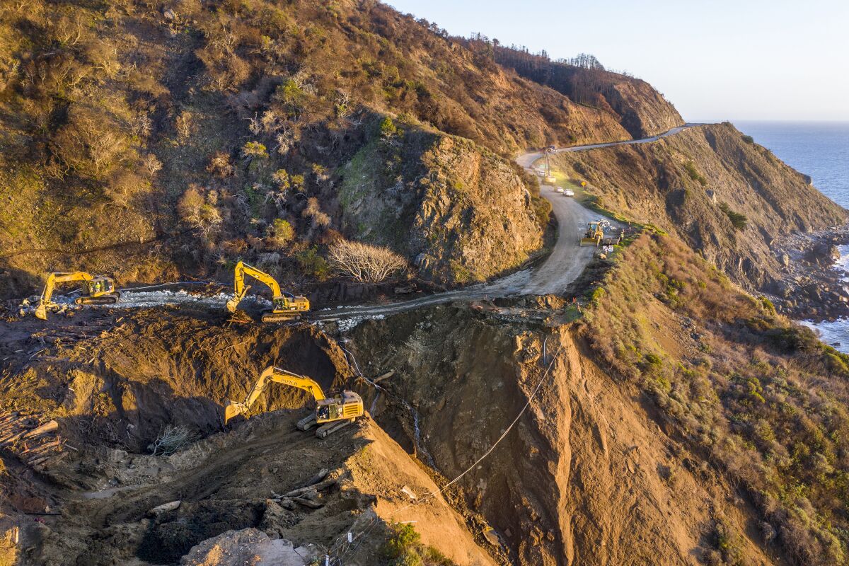 An aerial view of heavy equipment on a mountainous coastal road.