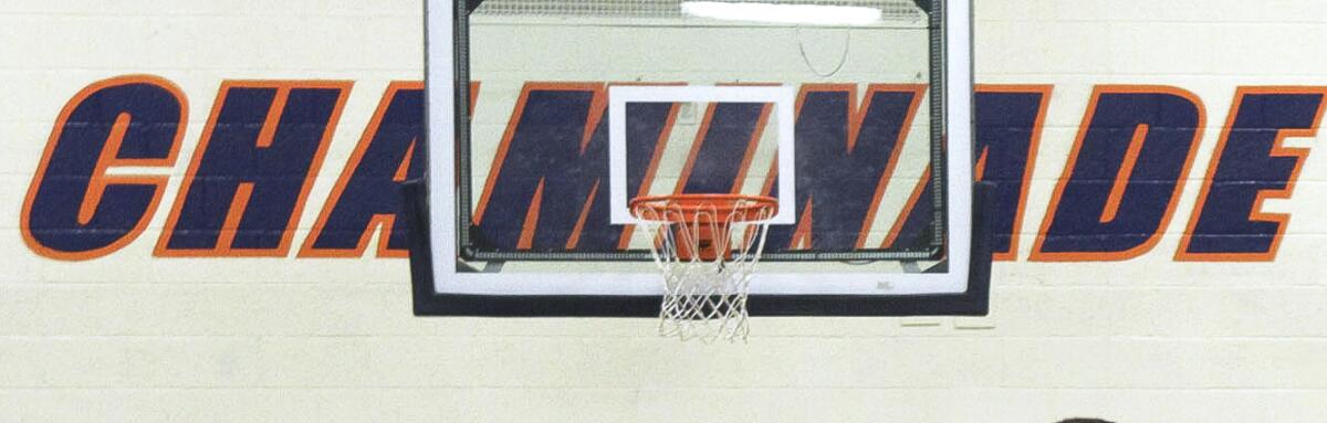 A basketball hoop and glass backboard, with the word "Chaminade" on a wall in the background
