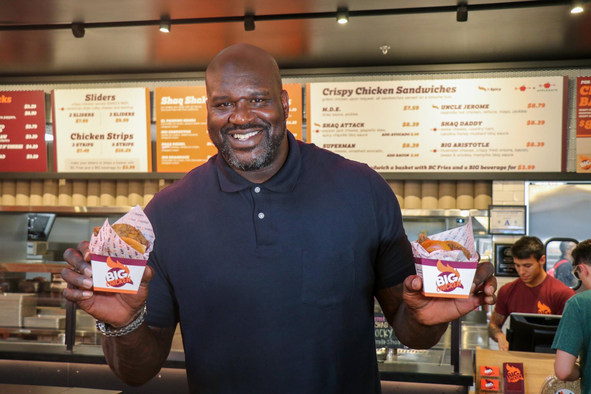Shaquille O'Neal's holds up samples of fried chicken from his chain restaurant 