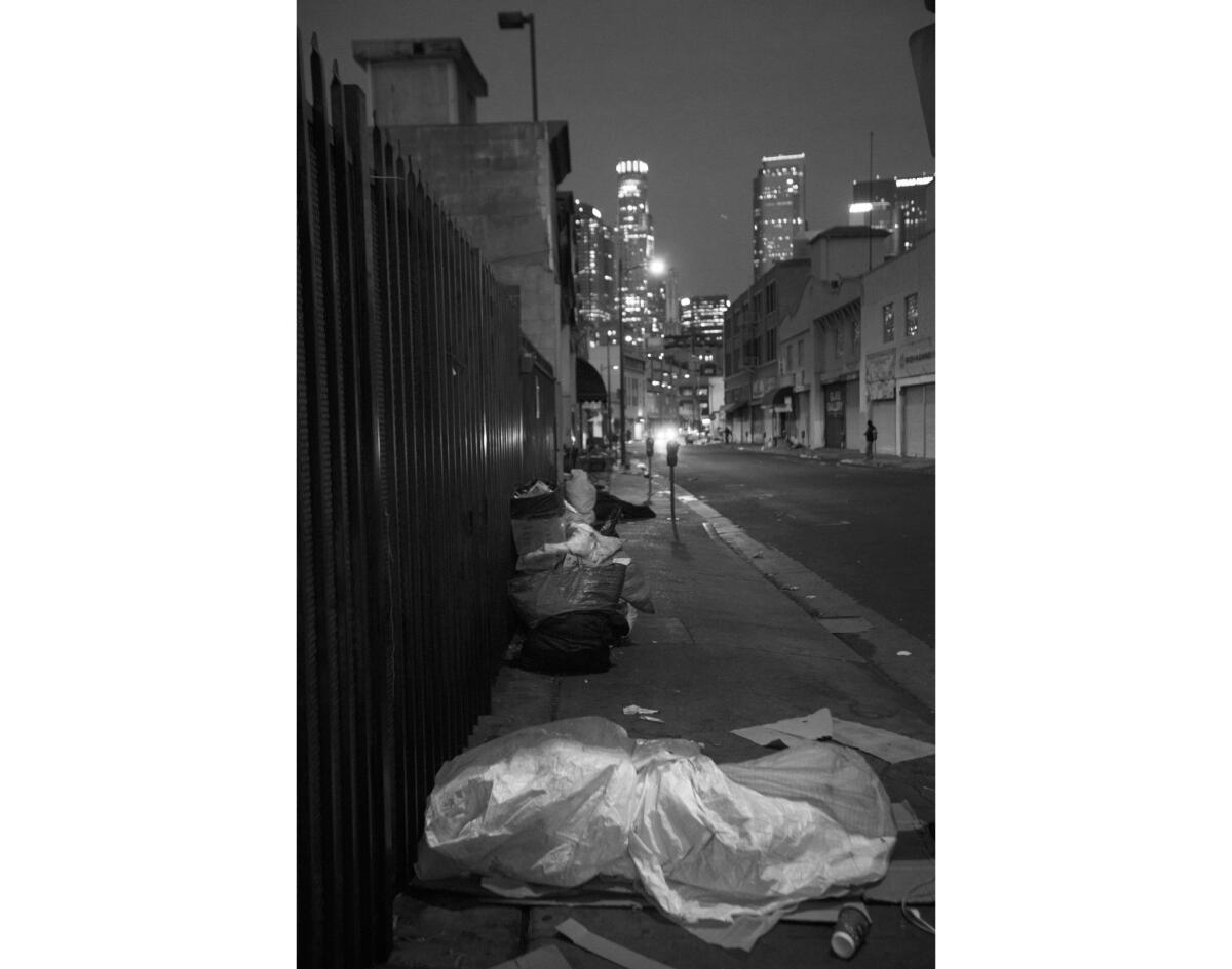 As dawn breaks, several people wrapped in tarps and covered with cardboard sleep along a sidewalk on Boyd Street.