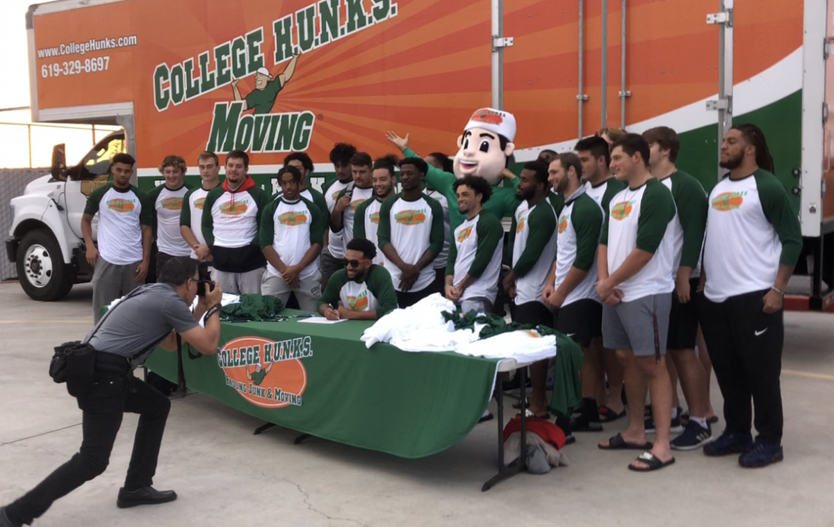 Football players pose with a College Hunks moving truck