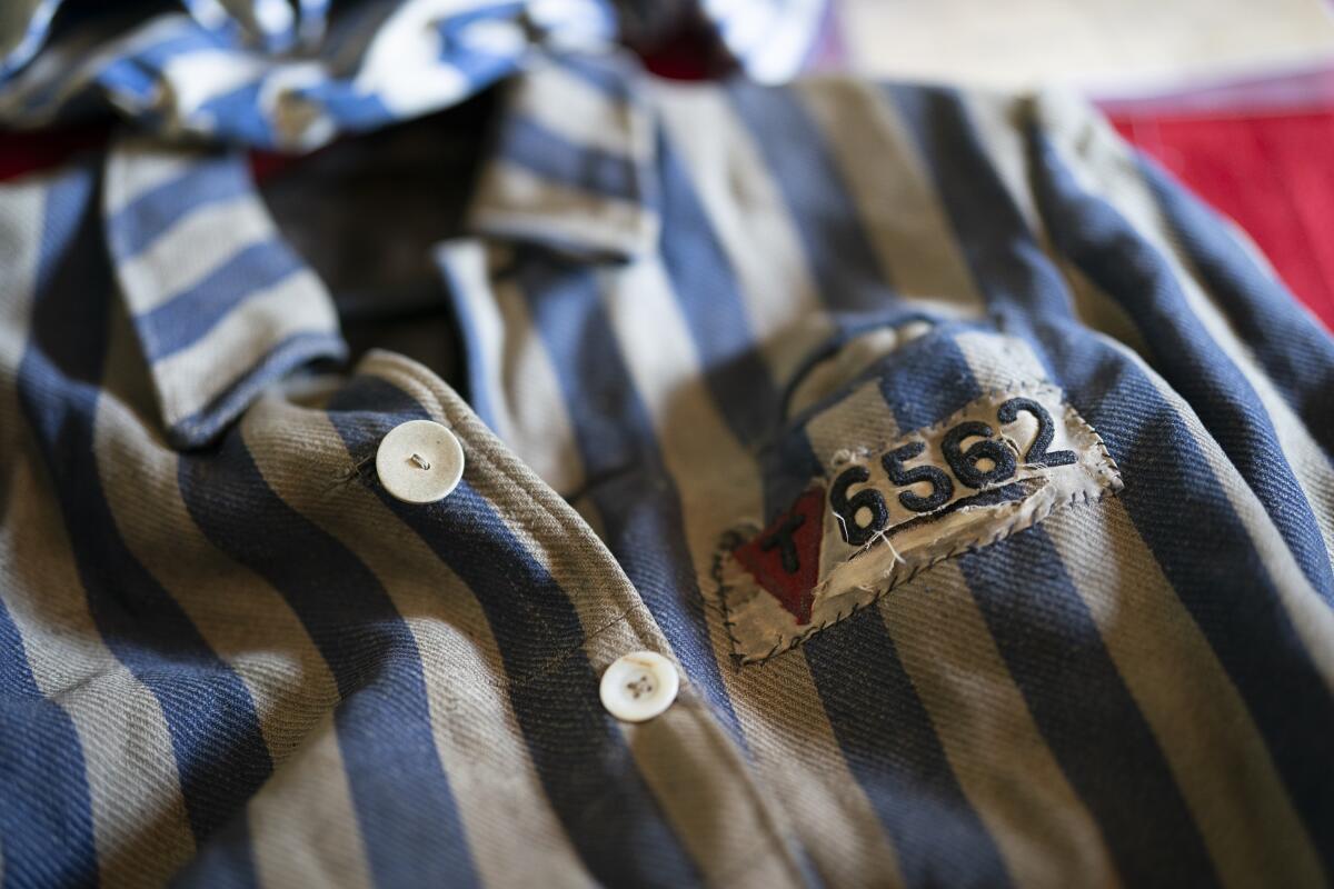 A close-up photo of a blue and white striped concentration camp uniform shirt, embroidered with numbers and a red triangle.