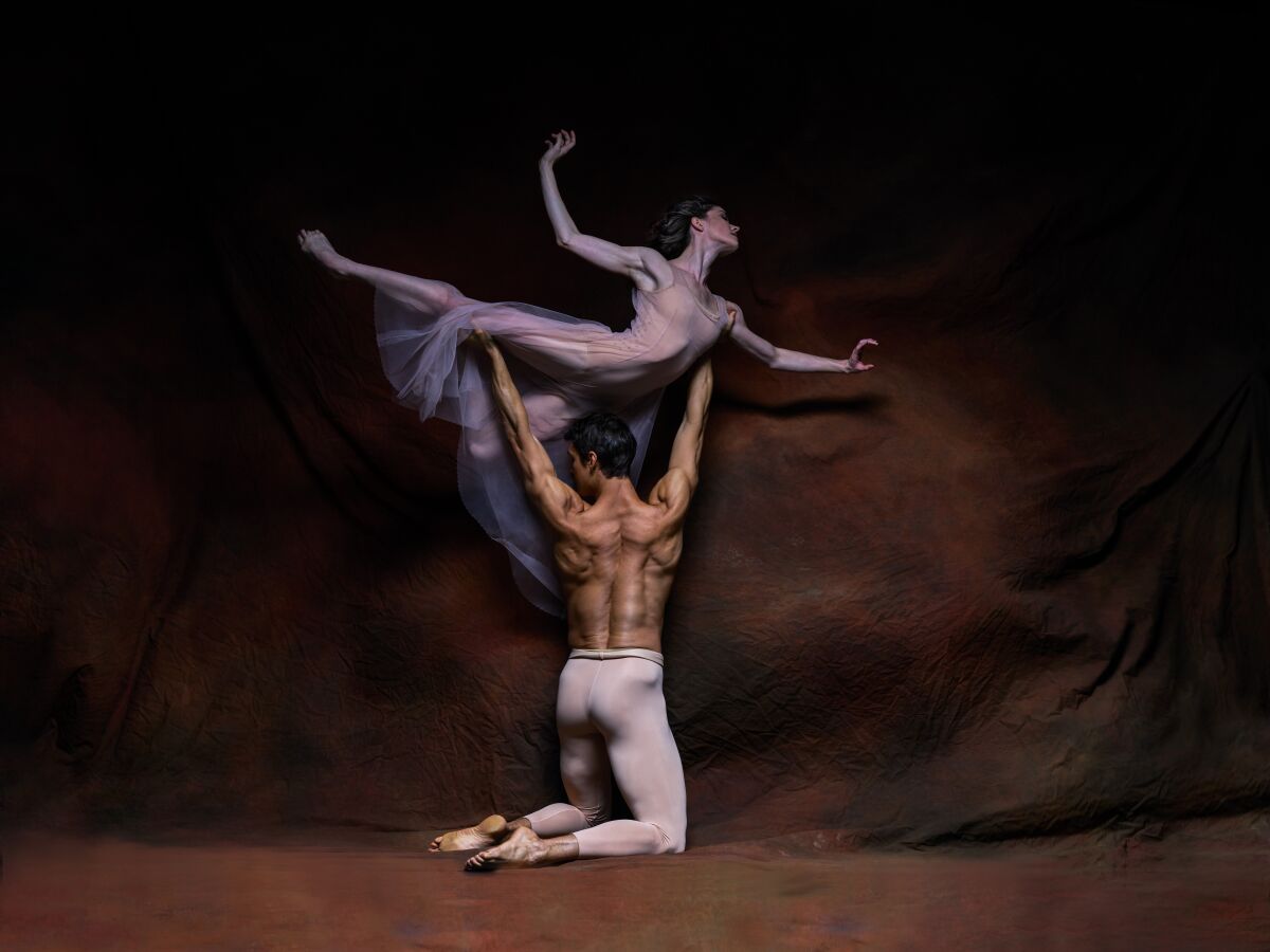 shirtless male ballerina holds up a female ballerina