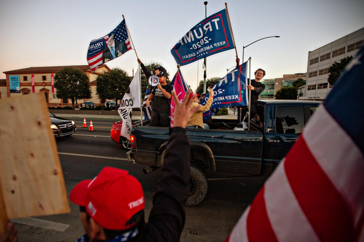 Supporters waving Trump flags ride in the back of a truck at a rally.
