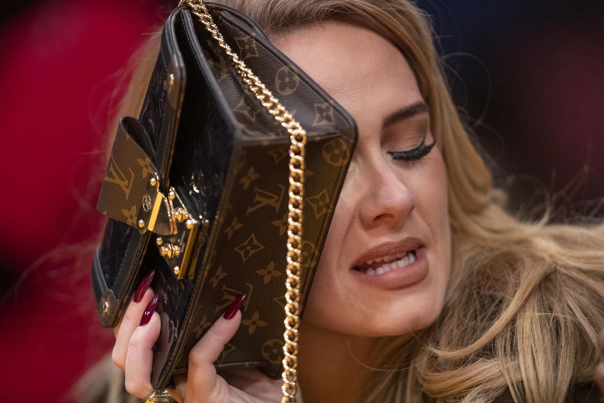 A woman hold up a purse with a gold chain to her face

