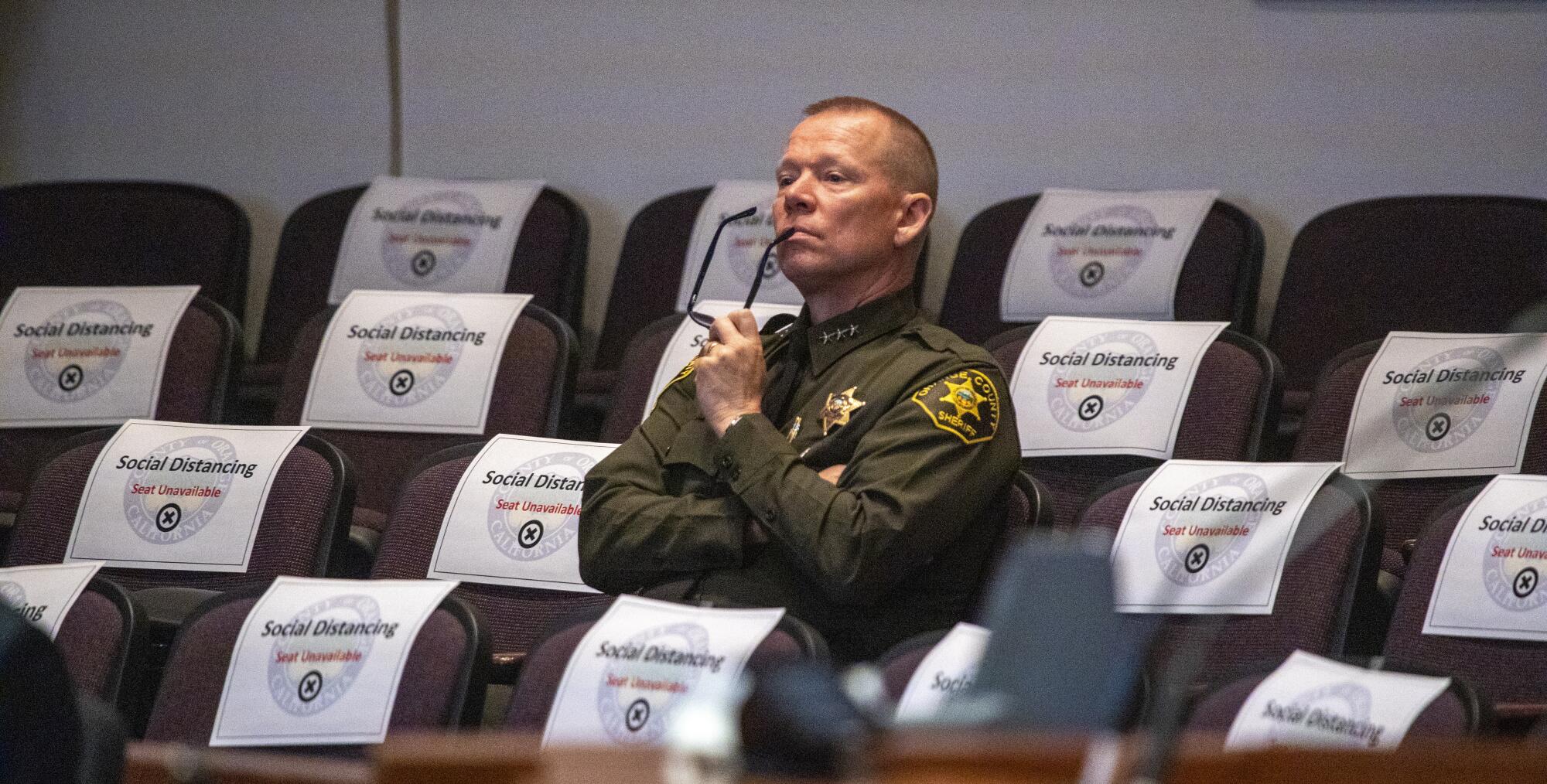 Surrounded by social distancing signs on seats, Orange County Undersheriff Bob Peterson listens to an official from the Orange County Health Care Agency describe to county supervisors the latest efforts to combat the coronavirus pandemic.