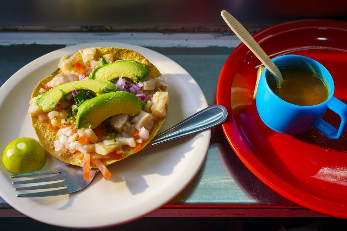 A taco on a white plate next to a small blue cup sitting on a red plate.