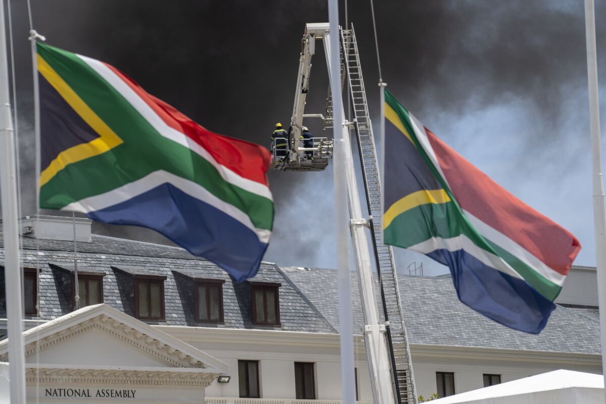 Firemen spray water on flames erupting from a building while flags fly in the foreground
