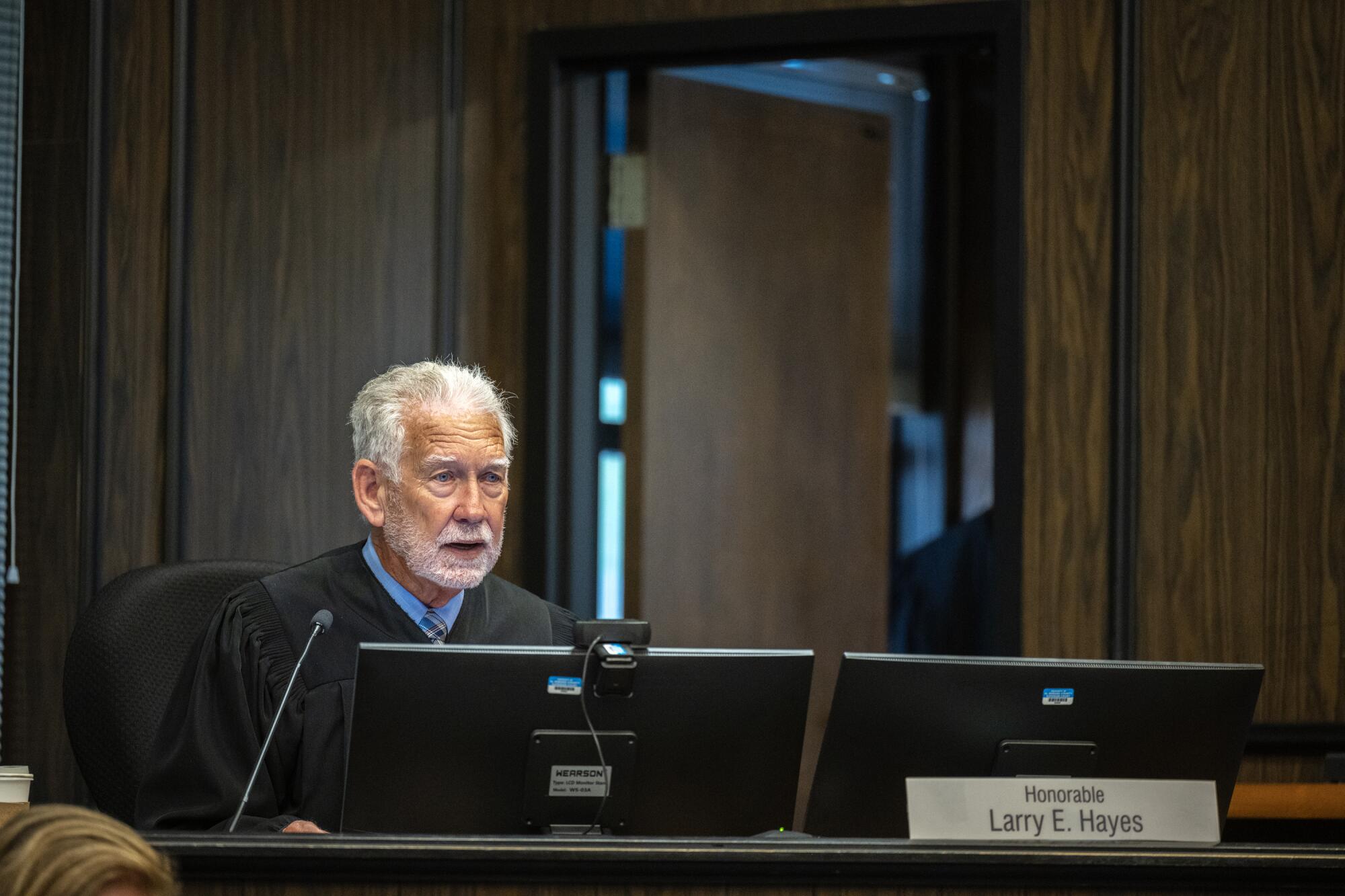 Judge Larry E. Hayes sits on the bench with two computer monitors and a microphone.