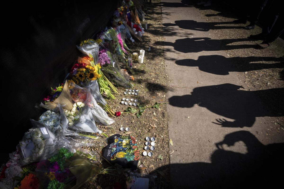 Visitors cast shadows next to a line of bouquets and candles.