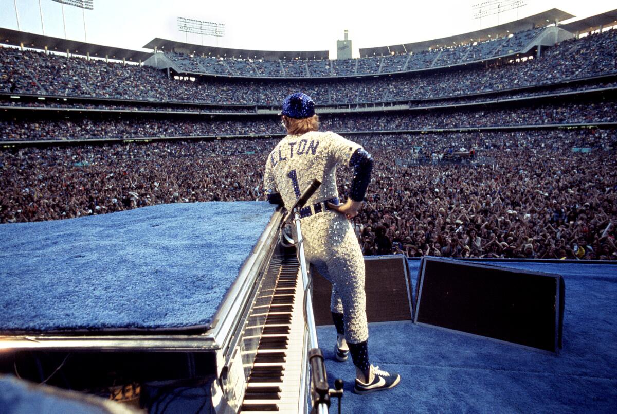 Elton John wears a sequined baseball uniform on a blue carpeted stage as he looked out at thousands of fans