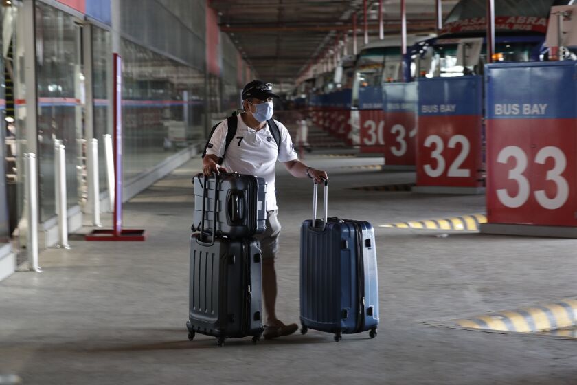 A Filipino seafarer pushes his bag at a bus terminal as he waits for a free bus ride in Paranaque, Metro Manila, Philippines, after spending weeks quarantined on a ship, Thursday May 28 2020. Seafarers were given a free ride to their provinces as the government continues to ease the lockdown which was set to prevent the spread of the new coronavirus in the country. (AP Photo/Aaron Favila)