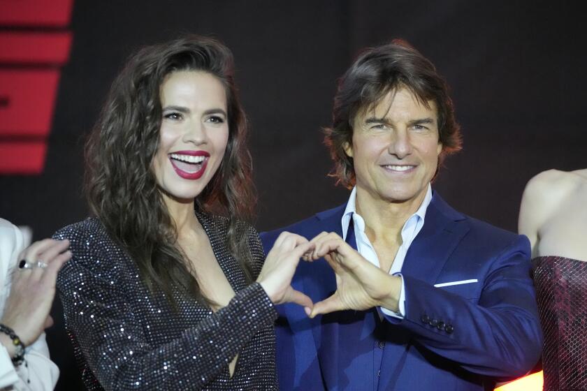 Hayley Atwell with curly hair and a black sparking dress and Tom Cruise in a blue suit forming a heart with their hands
