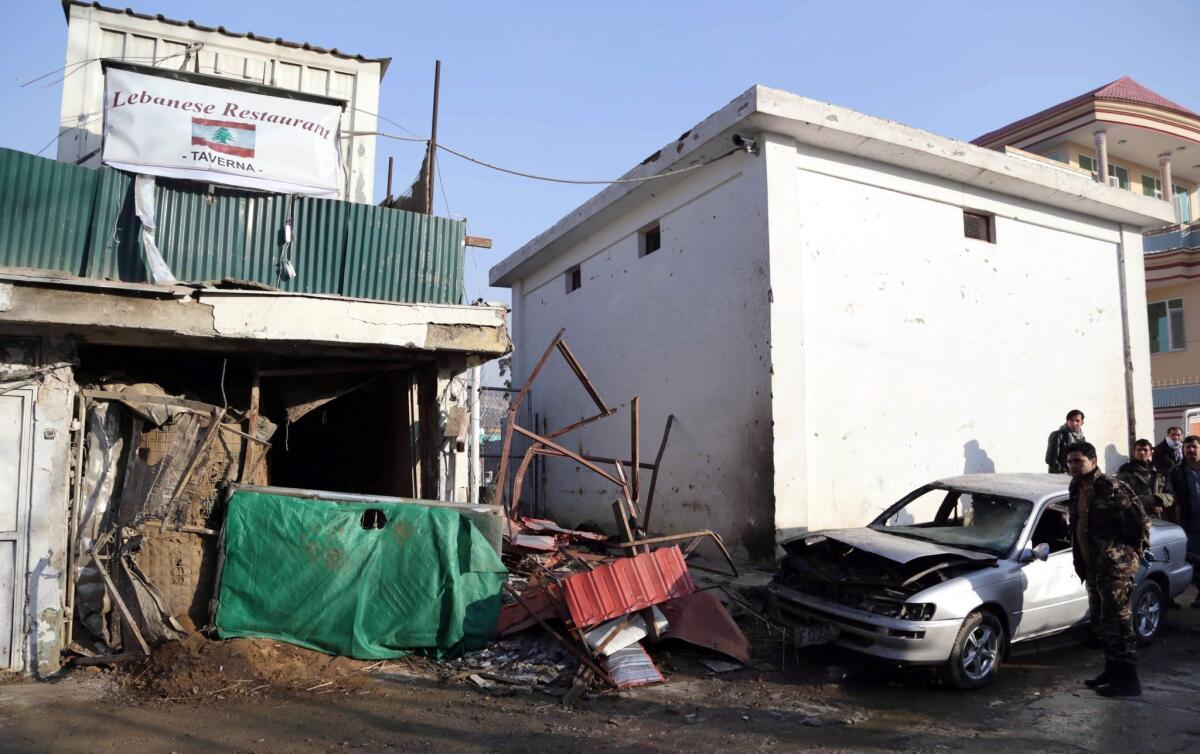 Afghan security officials stand guard Saturday outside the damaged entrance of a Lebanese restaurant that was attacked in Kabul, leaving 21 people dead, many of them foreigners.
