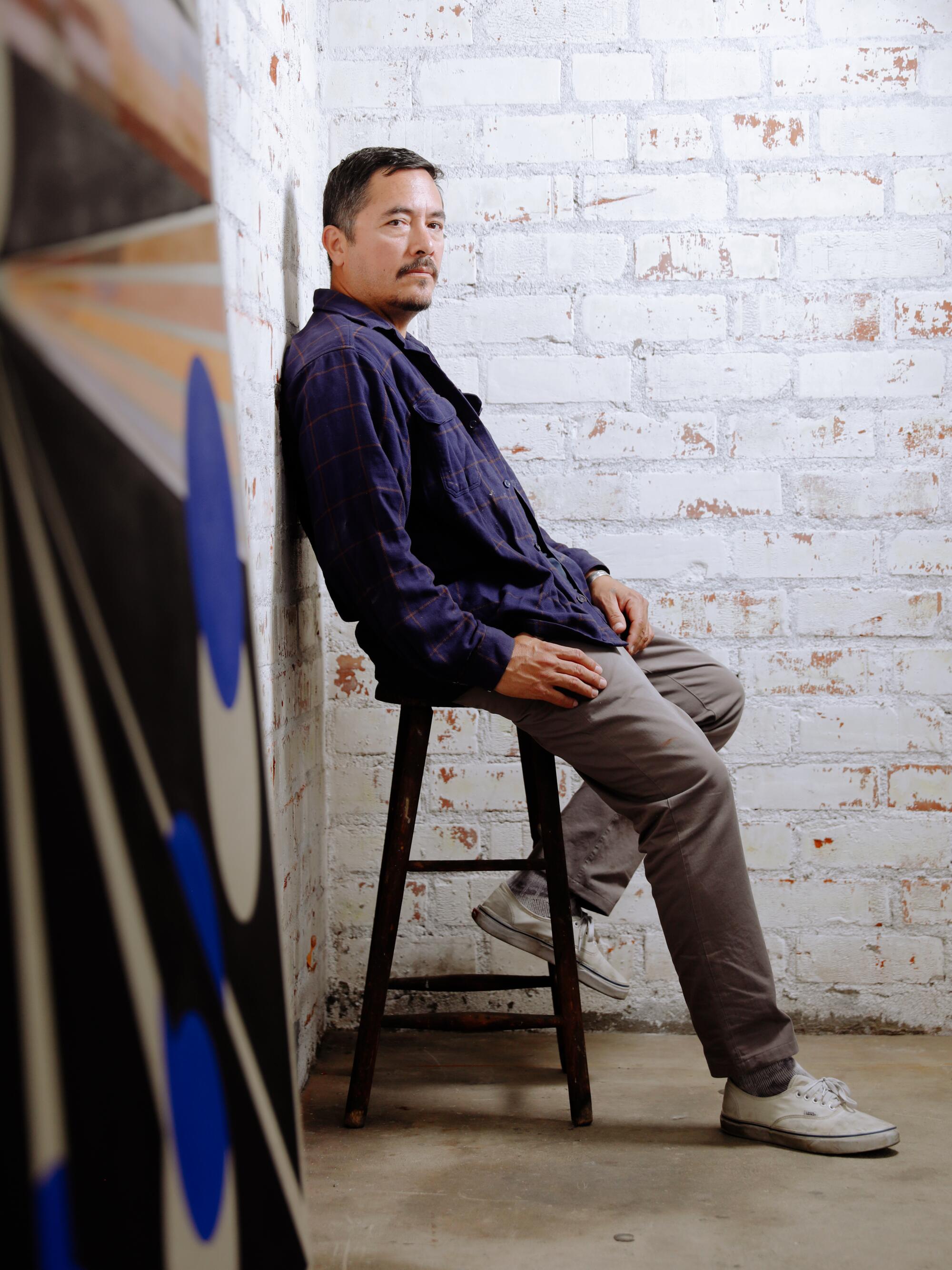 Eamon Ore-Giron sits on a bench while leaning against a wall in his studio in Los Angeles.