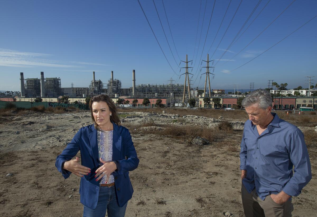 Hermosa Beach City Councilwoman Stacey Armato and Redondo Beach Mayor Bill Brand stand under power lines that carry electricity from the AES plant in Redondo Beach, seen in the background, left.