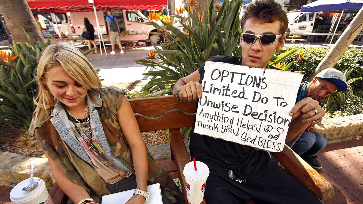 Daniella Hearn, 18, left, who grew up in Santa Barbara, with friend Frank "Wolv" Hunt, 20, from Georgia use signs written on cardboard to lure change from pedestrians as they walk by on State Street in Santa Barbara on Tuesday.