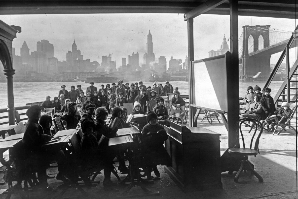 This 1911 photo from the Library of Congress shows schoolchildren on the ferry boat Rutherford, across the river from Manhattan, and near the Brooklyn Bridge, at right, in New York. Poor ventilation in school buildings across the U.S. will limit the ability of in-person instruction to resume safely. Some districts are warming to the idea of outdoor classrooms. (Library of Congress via AP)