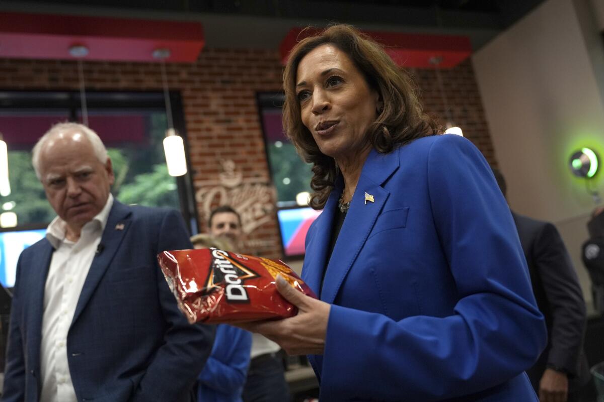 Democratic presidential nominee Kamala Harris holds a bag of Doritos as her running mate, Tim Walz looks on.