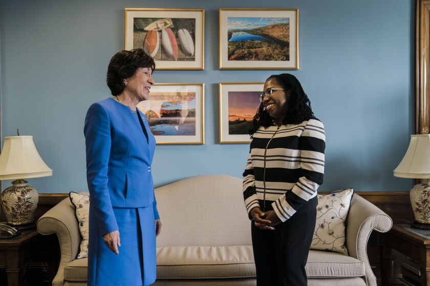 a woman in a blue suit greets a woman with glasses and a black and white striped jacket