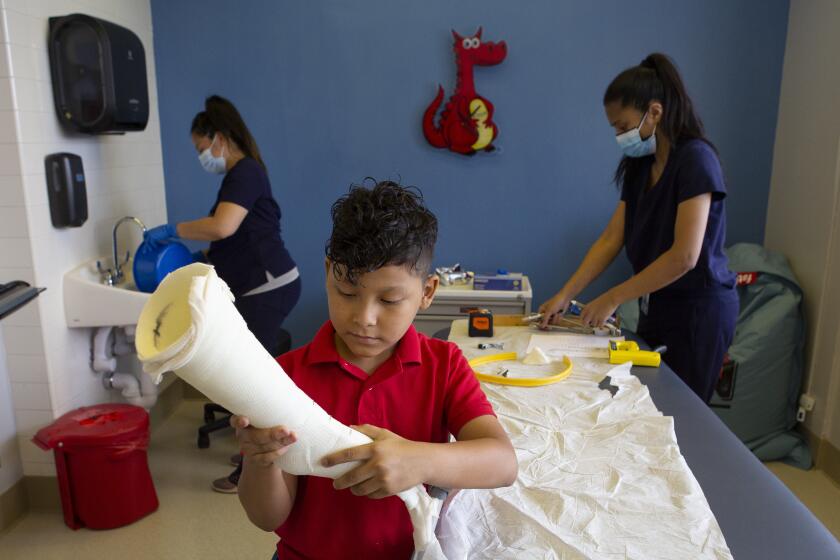 Los Angeles, CA - August 18: Orthotists Courtney Tolentino (right) and Natalie Wilson (left) stand behind Efran as he examines a cast of his leg on Wednesday, Aug. 18, 2021, at UCLA Health in Los Angeles, CA. (Madeleine Hordinski / Los Angeles Times)