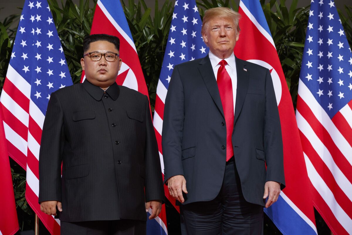 North Korean President Kim Jong Un stands formally in front of flags next to then-U.S. President Donald Trump