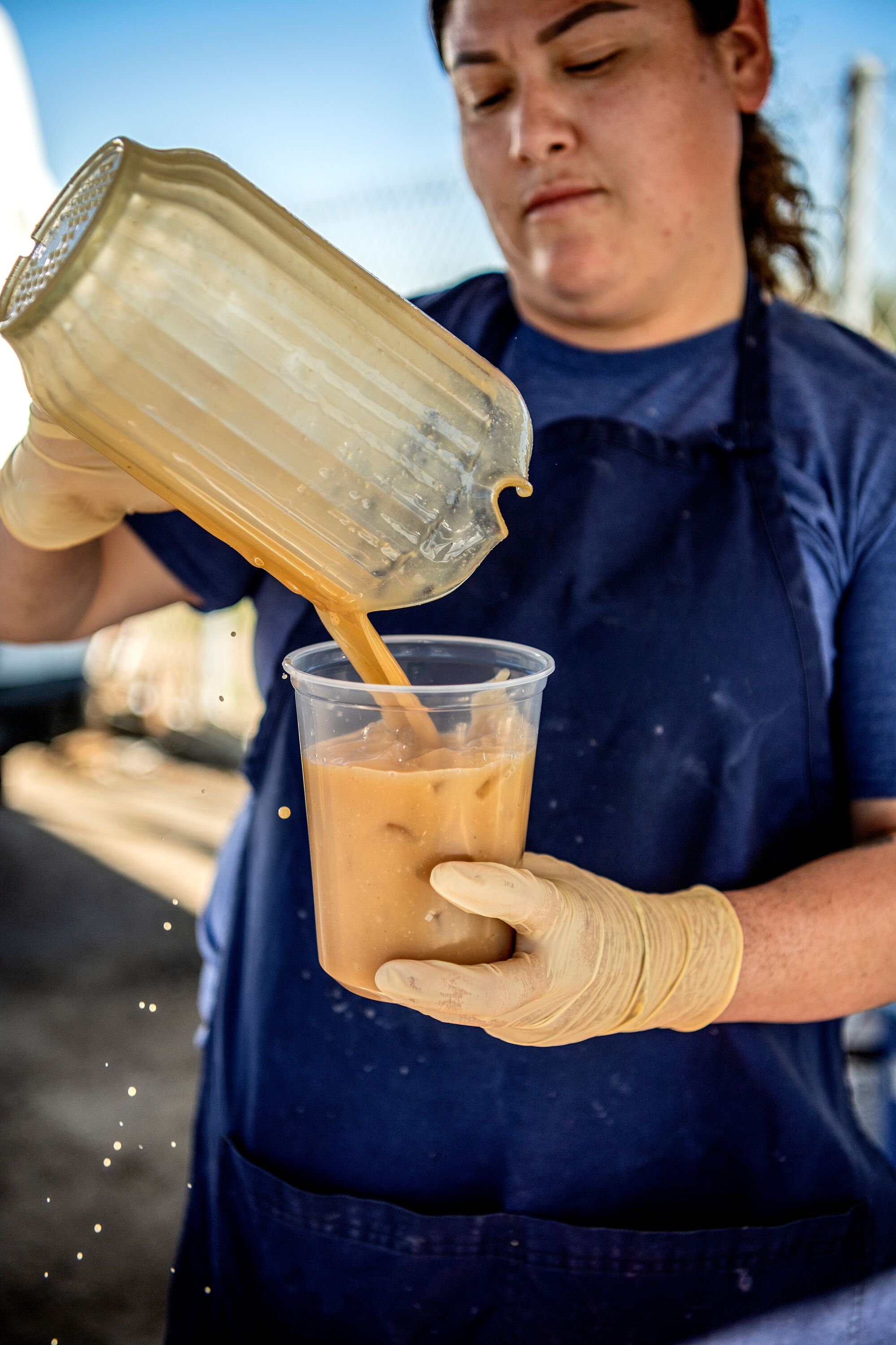 A woman pours tejuino from a pitcher into a cup.
