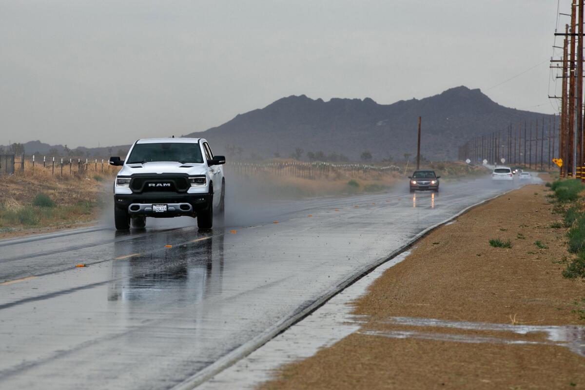 A pickup truck kicks up spray on a desert highway, followed by a sedan in the distance. 