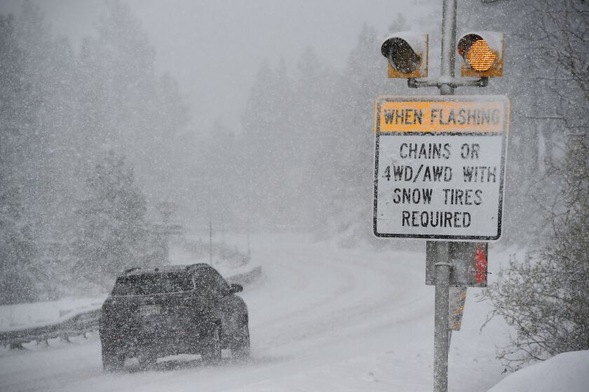 A car passes a caution sign as heavy snow falls on the Mt. Rose Highway near Reno, Nev., on Dec. 1, 2022. A windy, winter storm packing heavy snow started moving into the Sierra Thursday, closing schools at Lake Tahoe, prompting a backcountry avalanche warning and snarling traffic on Interstate 80 west of Reno. (Jason Bean/Reno Gazette-Journal via AP)
