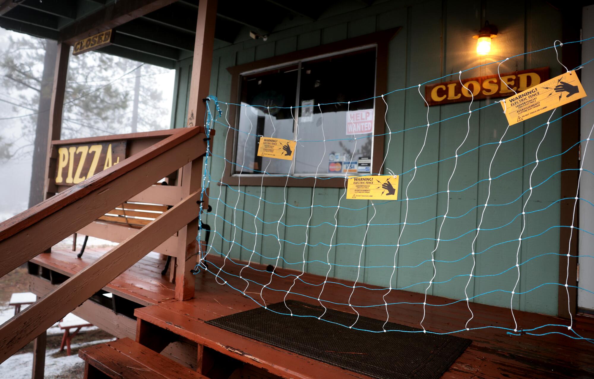 A net hangs across the porch entrance of a pizza restaurant with a Closed sign and a light on