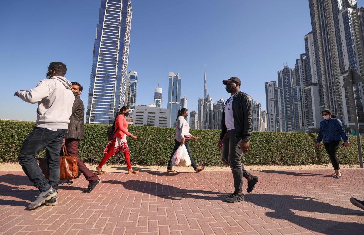 Workers walking in Dubai with skyscrapers in the background.