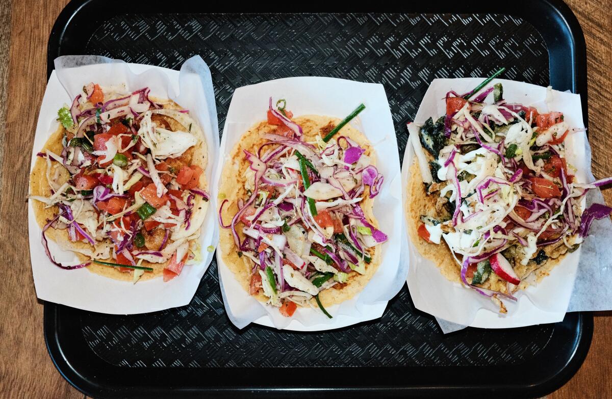 A trio of tempura-battered tacos topped with cabbage and pico de gallo on a black plastic tray at Three Flames in Westchester