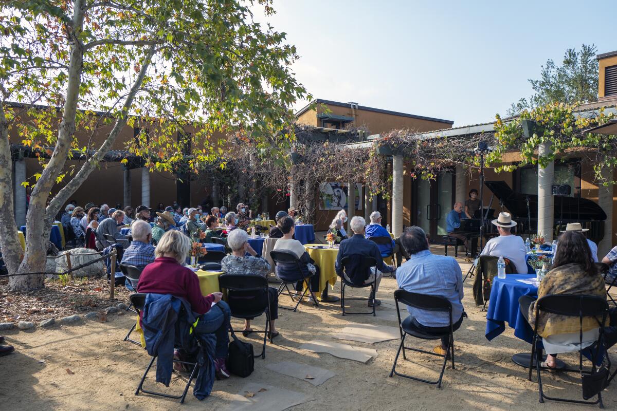 People seated on folding chairs outdoors at Audubon Center at Debs Park listen to a pianist.