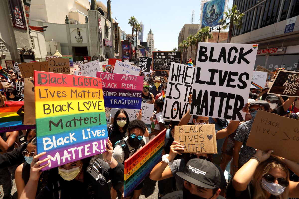 People hold up various Black Lives Matter signs in a street.