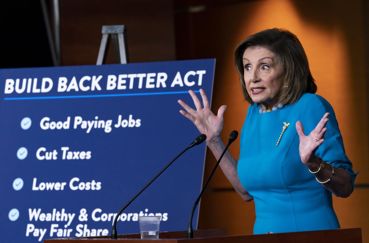 House Speaker Nancy Pelosi speaks as she stands by a poster with bullet points about the Build Back Better bill. 