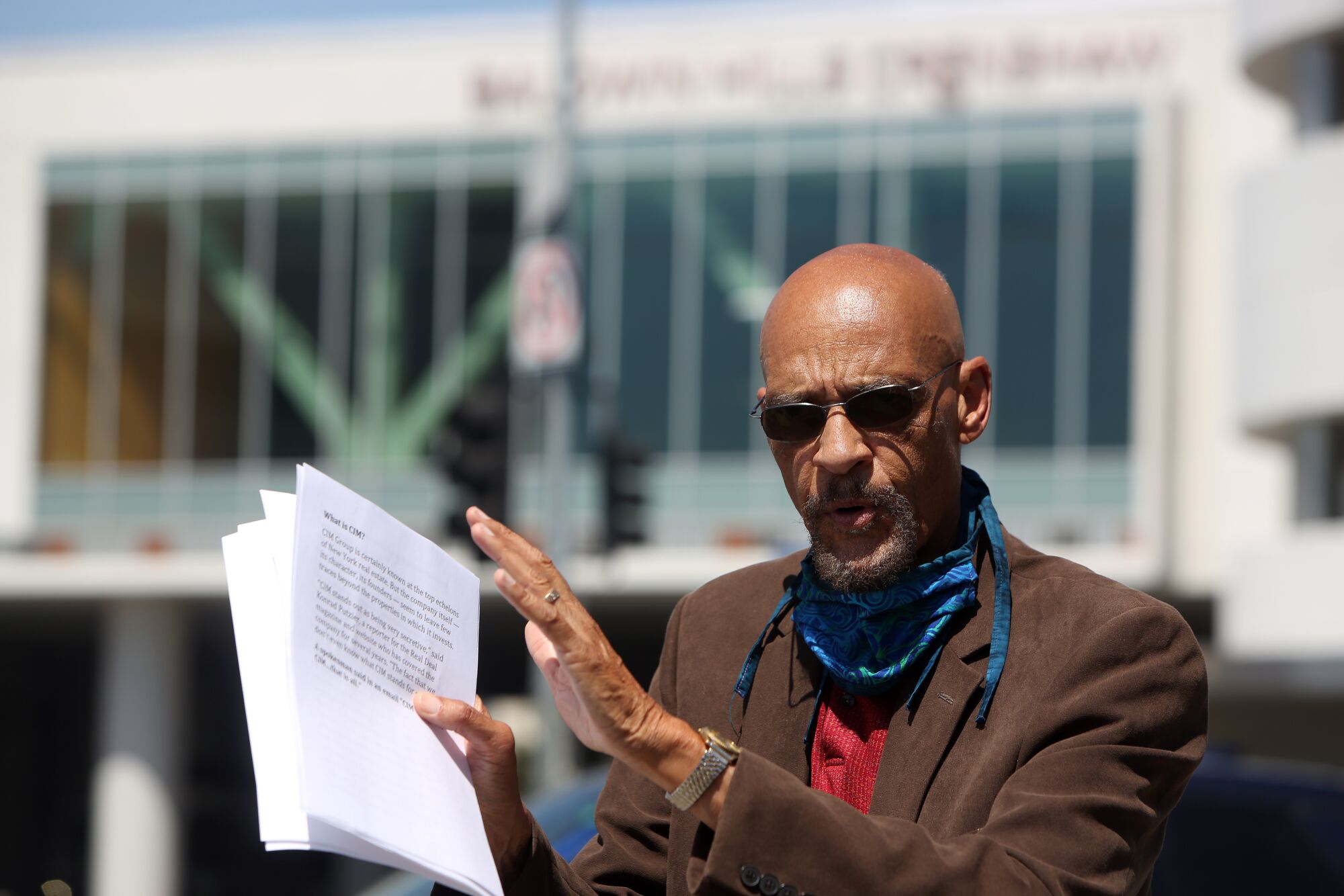 A man holding papers speaks outside a shopping center.