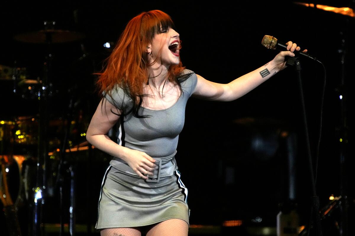 Hayley Williams of Paramore sings onstage with her hands held out to her sides.