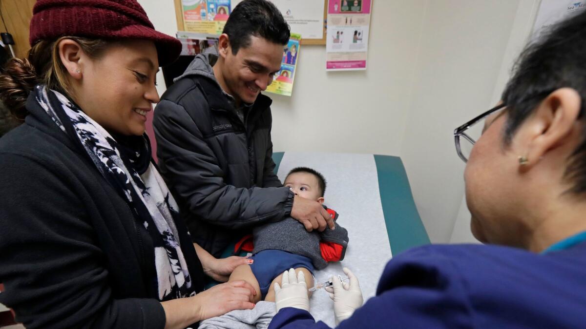 Matilde Gonzalez, left, and Cesar Calles of Seattle hold their 10-month-old son, Cesar, as medical assistant Ana Martinez gives him a flu shot at their local community health center. But how long will the clinic stay open in the face of a congressional funding shutoff?