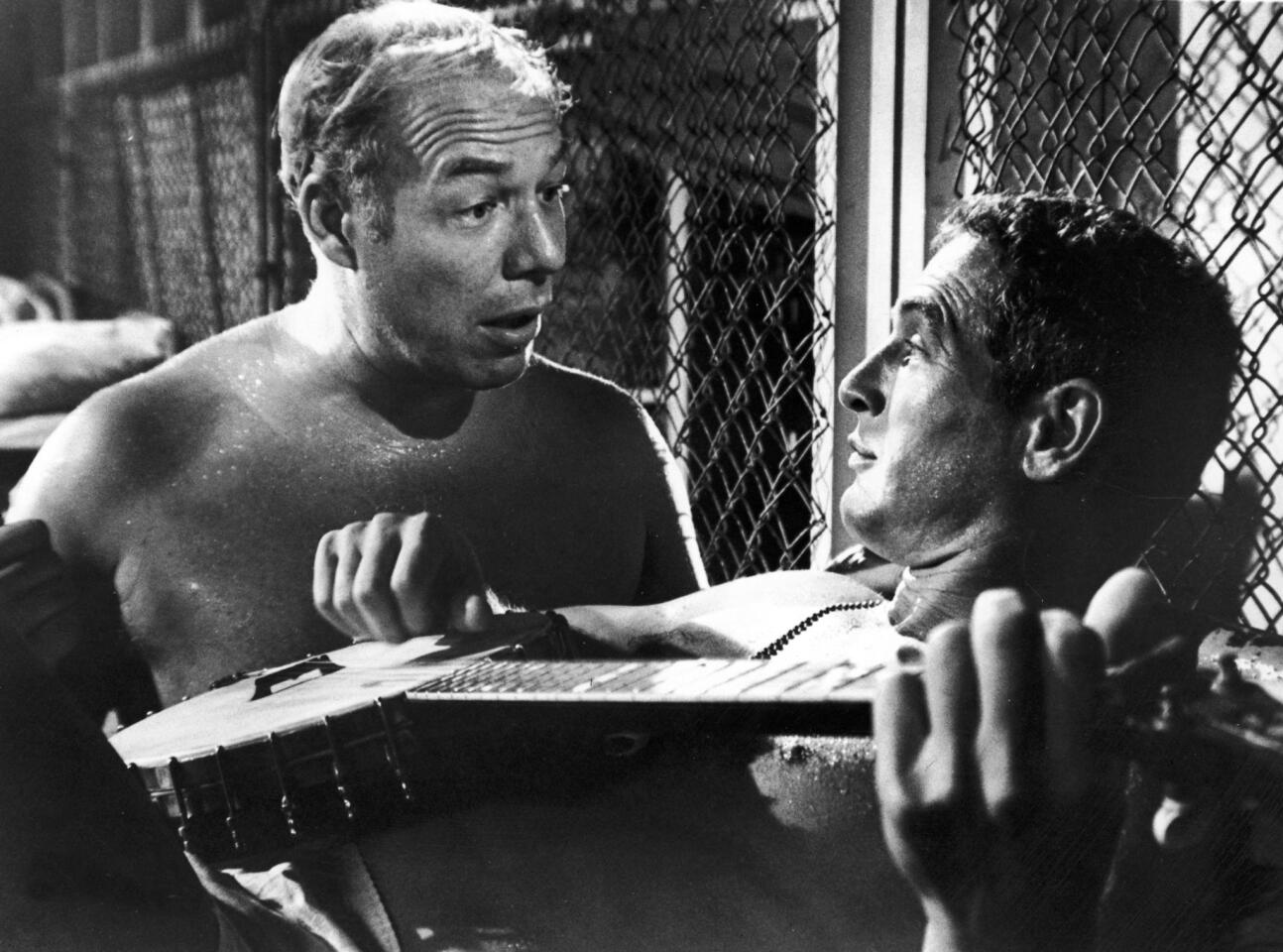 Paul Newman, playing a banjo, and George Kennedy in the film "Cool Hand Luke" directed by Stuart Rosenberg. Newman won a best actor Oscar, and Kennedy won a best supporting actor Oscar for their roles in the film.
