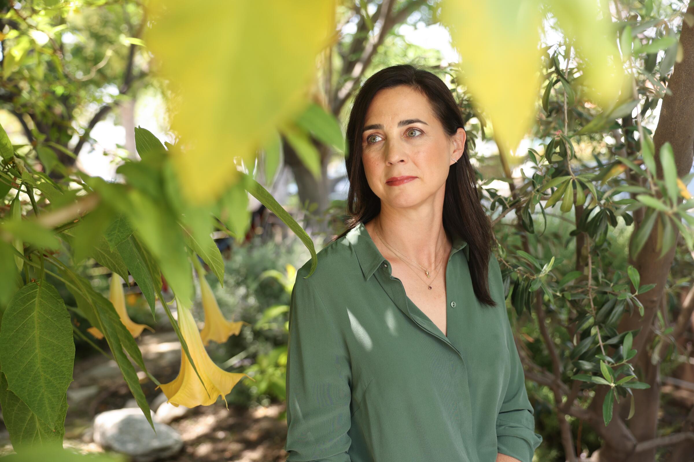 A woman in a green shirt surrounded by green leaves from nearby trees
