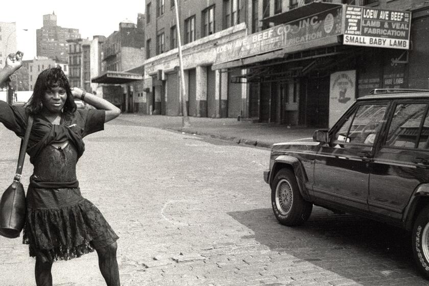 A woman in a dark dress with a purse slung over her shoulder standing on a New York street.