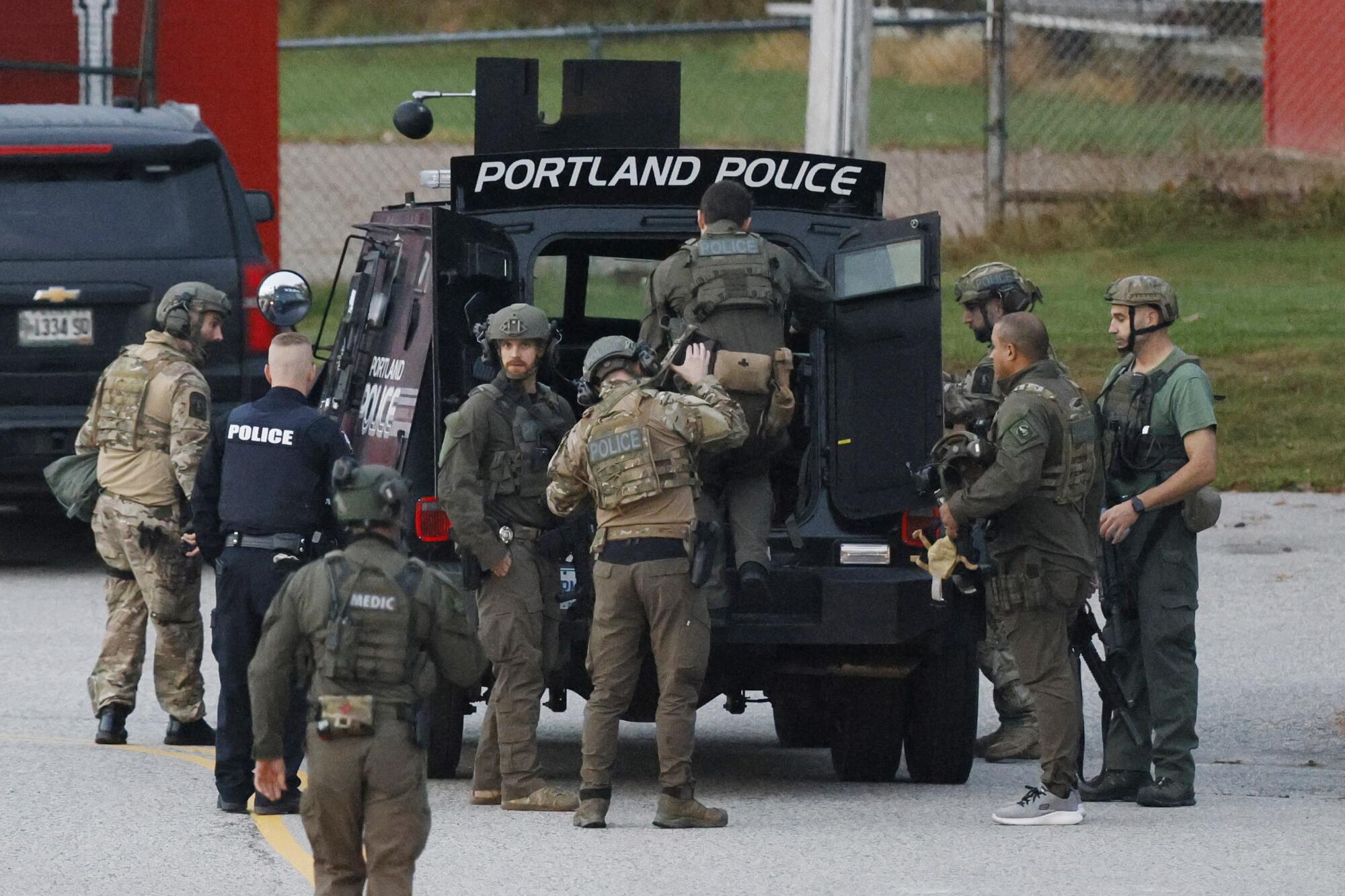 Several law enforcement officers in tactical gear gathering around the open back end of vehicle labeled "Portland Police."