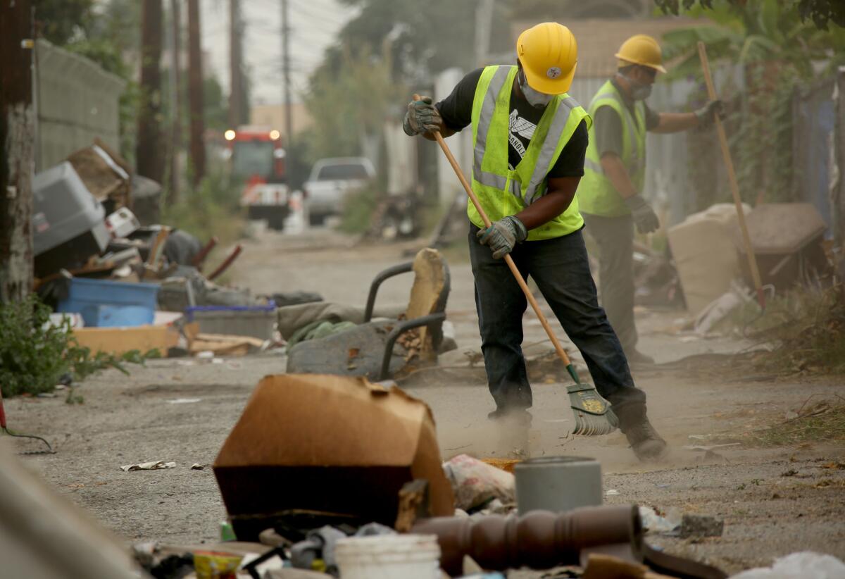 City sanitation workers Erik Scott, left, and Cesar Galvez clean illegally dumped trash from an alley in the Green Meadows neighborhood of South Los Angeles in May 2015.