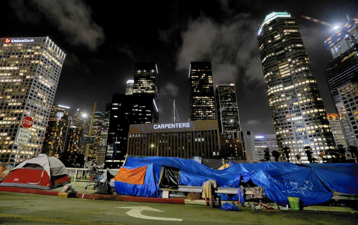 A homeless man prepares to sleep for the night in a streetside encampment beneath the gleaming towers of the financial district in downtown Los Angeles.