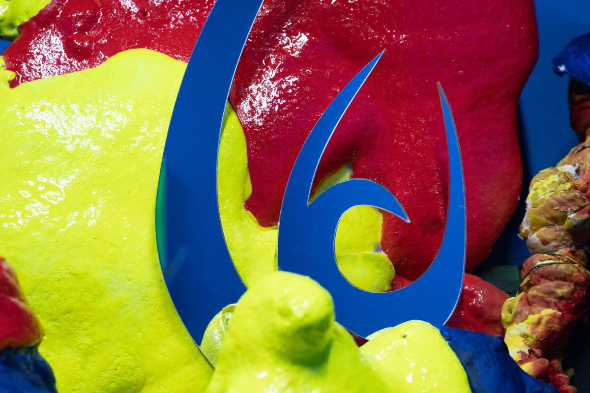 A close-up reveals hardened, plastic forms in strange shades of blue red and yellow, on which sits a piece of carved plastic.