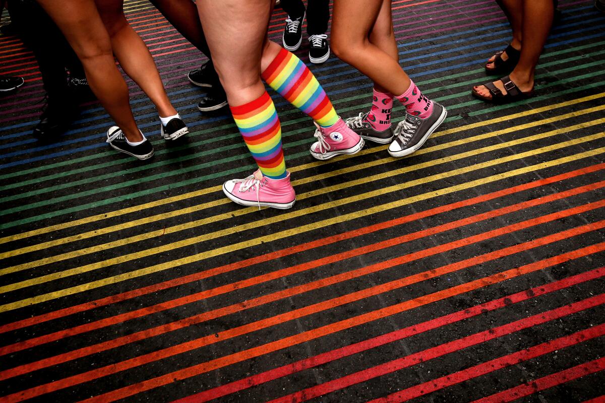 A woman wearing rainbow-colored socks walks across a rainbow-colored crosswalk. 