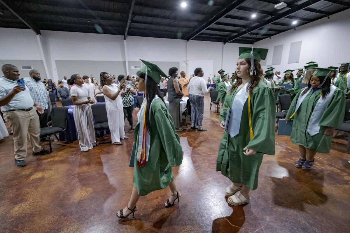 Students graduate in green caps and gowns.