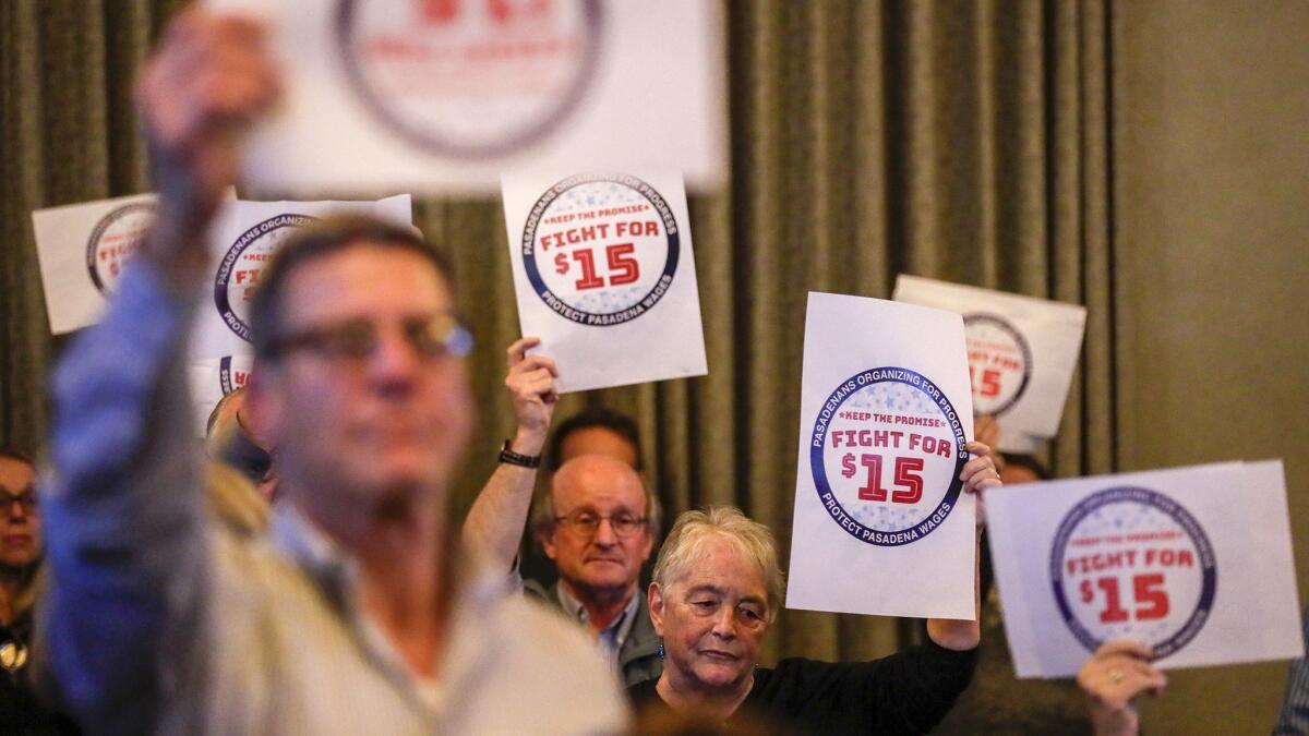Dozens of people hold signs advocating for an accelerated planned increase of the minimum wage at the Pasadena City Council meeting.