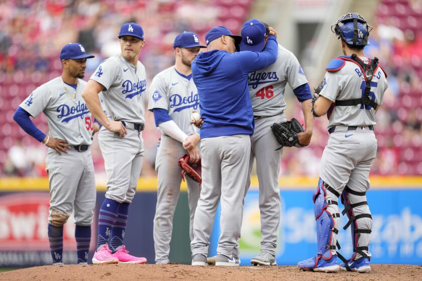 Los Angeles Dodgers pitcher Yohan Ramírez (46) is embraced by manager Dave Roberts, third from right, after he hit Cincinnati Reds' Stuart Fairchild with a throw during the eighth inning of a baseball game Sunday, May 26, 2024, in Cincinnati. (AP Photo/Jeff Dean)